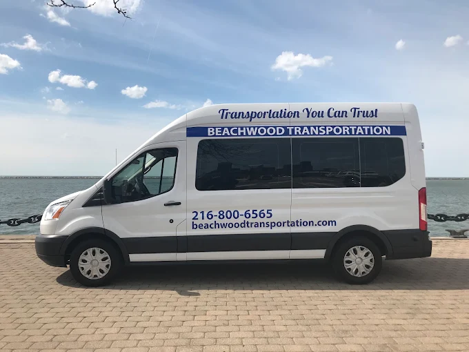 White passenger van with Beachwood Transportation branding parked along a waterfront boardwalk with the ocean in view.